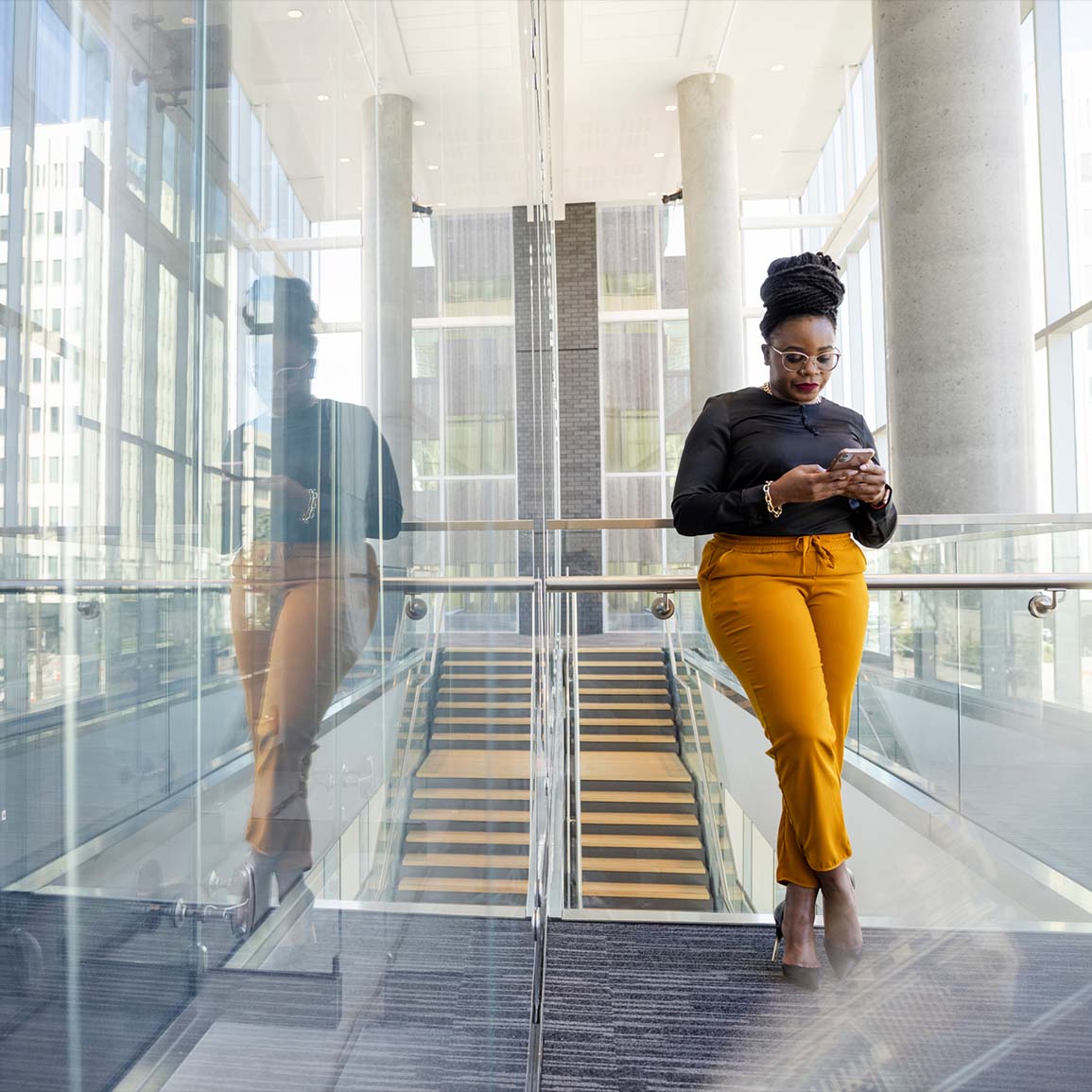 Female business owner leaning on wall, reading resource on her phone